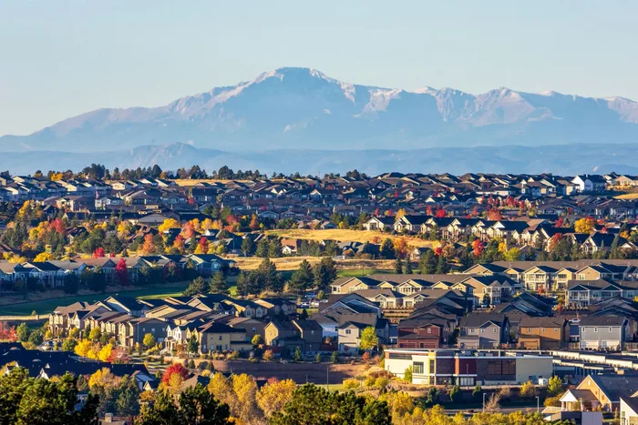 Aerial view of a suburban neighborhood in autumn with a snow-capped mountain range on the horizon